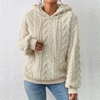 Femme portant un pull à capuche en laine beige texturée, motif chevrons, manches longues, associé à un jean bleu. Mode automne-hiver tendance.