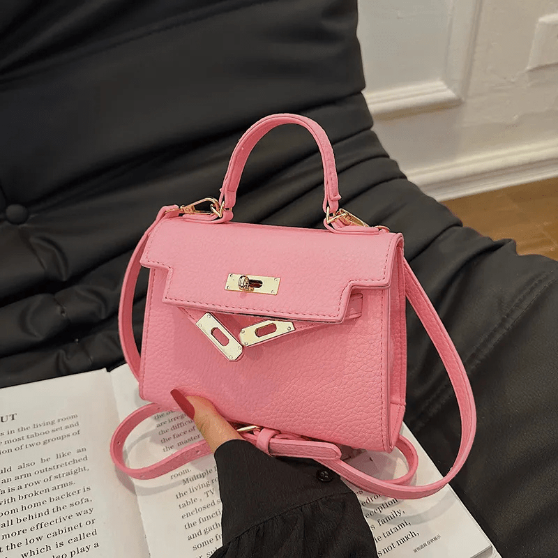 Sac à main rose élégant sur canapé noir, design moderne avec fermoir métallique, idéal pour mode féminine et accessoires tendance.