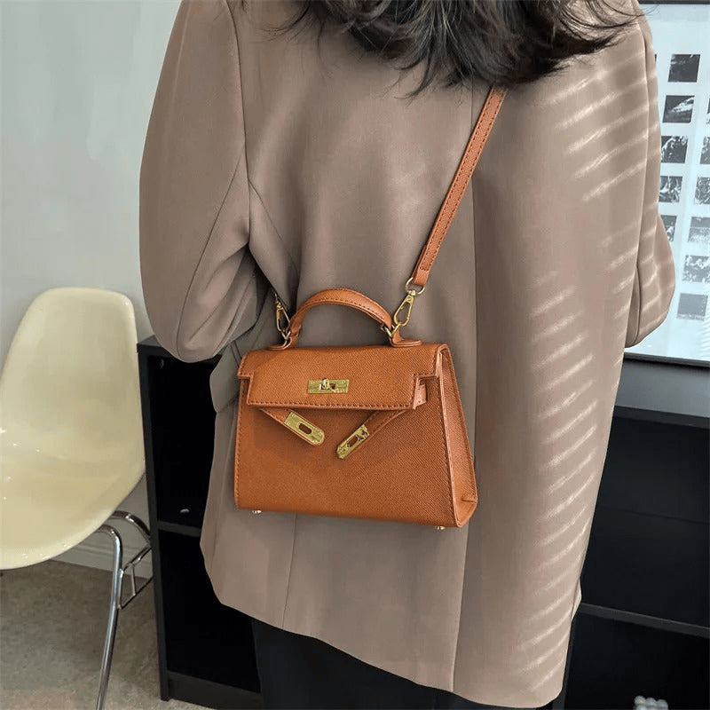 Femme portant un sac à main en cuir marron de style Birkin, avec une bandoulière, sur un manteau beige. Mode élégante et accessoires de luxe.