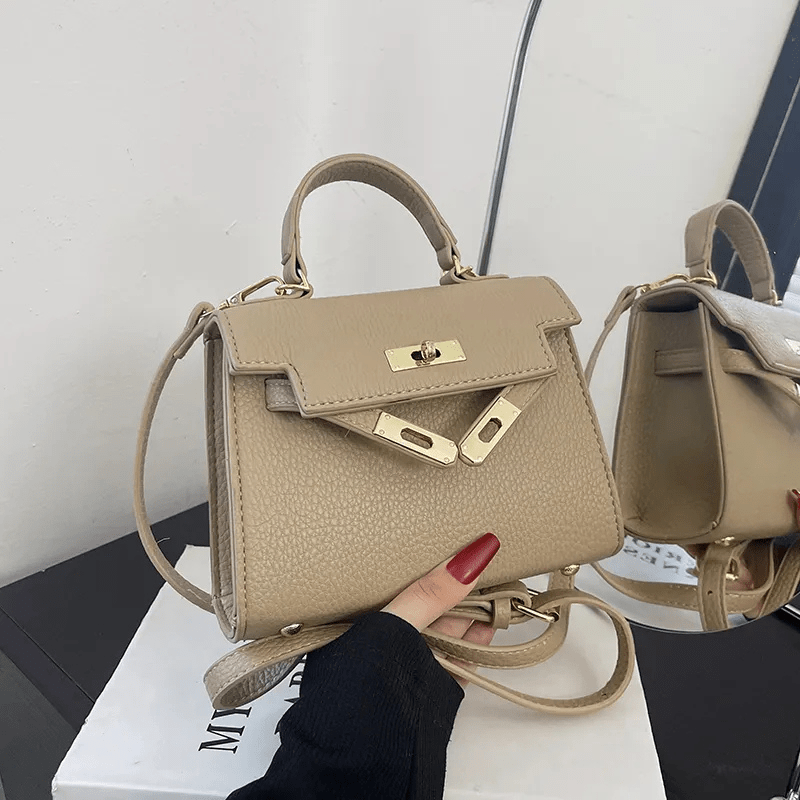 Sac à main beige élégant avec poignée supérieure, fermoir doré et bandoulière ajustable, posé sur une boîte blanche. Accessoire mode tendance.