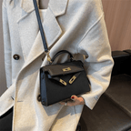 Sac à main noir élégant avec détails dorés, porté par une personne en manteau beige. Mode féminine, accessoire chic, tendance automne-hiver.