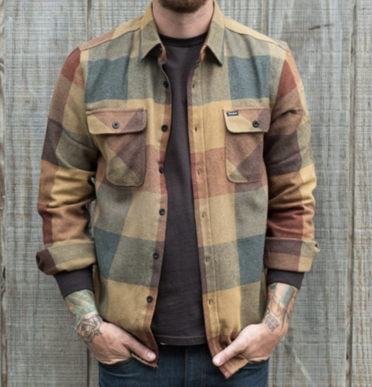 Homme portant une chemise à carreaux en flanelle multicolore, manches longues, devant un mur en bois. Mode masculine décontractée, style automnal.