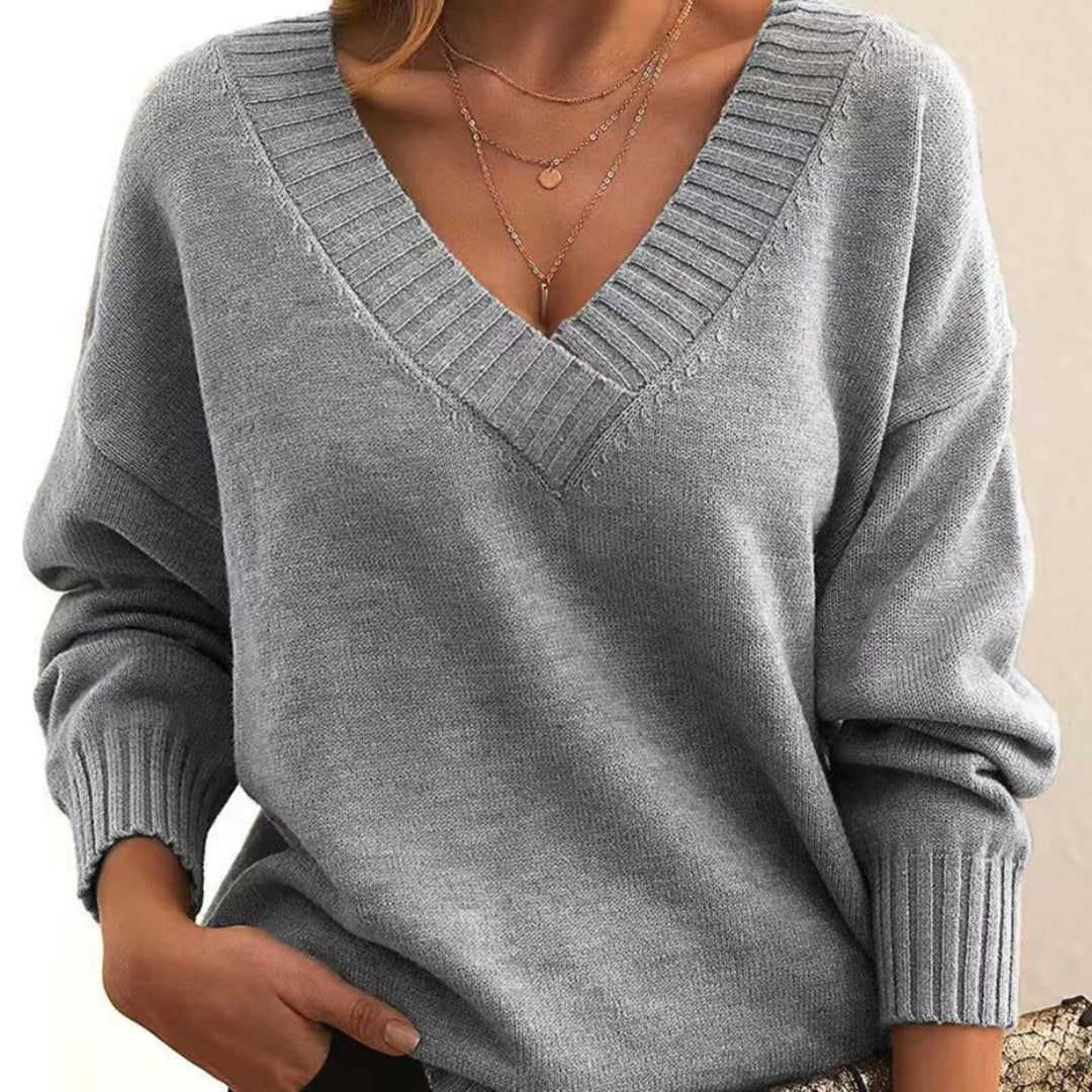 Femme portant un pull gris à col en V, manches longues, avec col côtelé. Style décontracté et élégant, idéal pour l'automne et l'hiver.