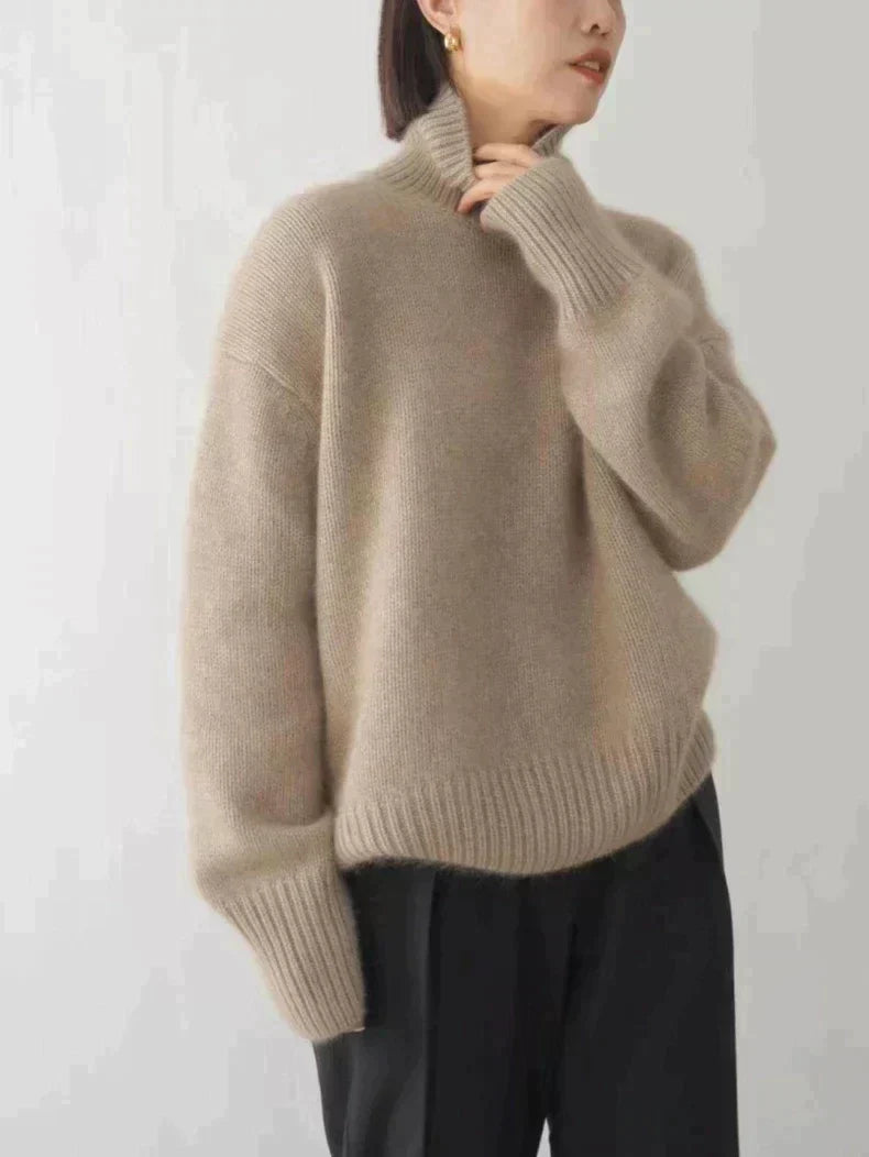 Femme portant un pull en laine beige à col roulé, manches longues, associé à un pantalon noir. Mode automne-hiver, style décontracté et élégant.