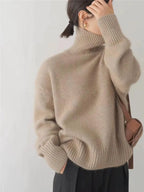 Femme portant un pull en laine beige à col roulé, manches longues, avec un sac marron. Mode automne-hiver, style décontracté et élégant.