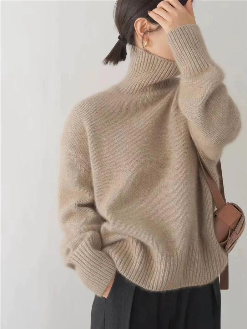 Femme portant un pull en laine beige à col roulé, manches longues, avec un sac marron. Mode automne-hiver, style décontracté et élégant.