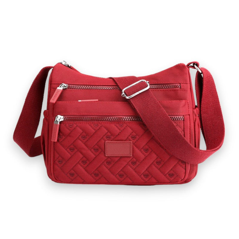 Sac à bandoulière rouge en tissu matelassé avec plusieurs poches zippées, design élégant et moderne, idéal pour un usage quotidien.