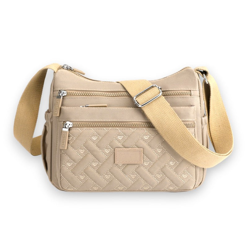 Sac à bandoulière beige en tissu matelassé avec poches zippées et sangle ajustable. Élégant et pratique pour un usage quotidien.