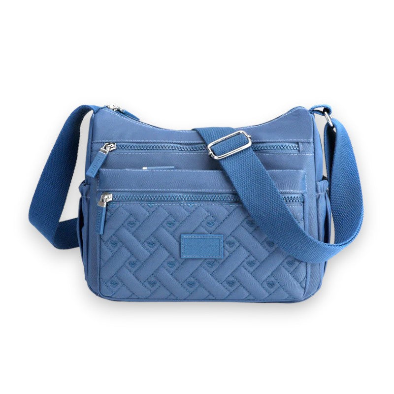 Sac bandoulière bleu en tissu matelassé avec motifs géométriques, trois poches zippées, sangle ajustable. Accessoire mode pratique et tendance.