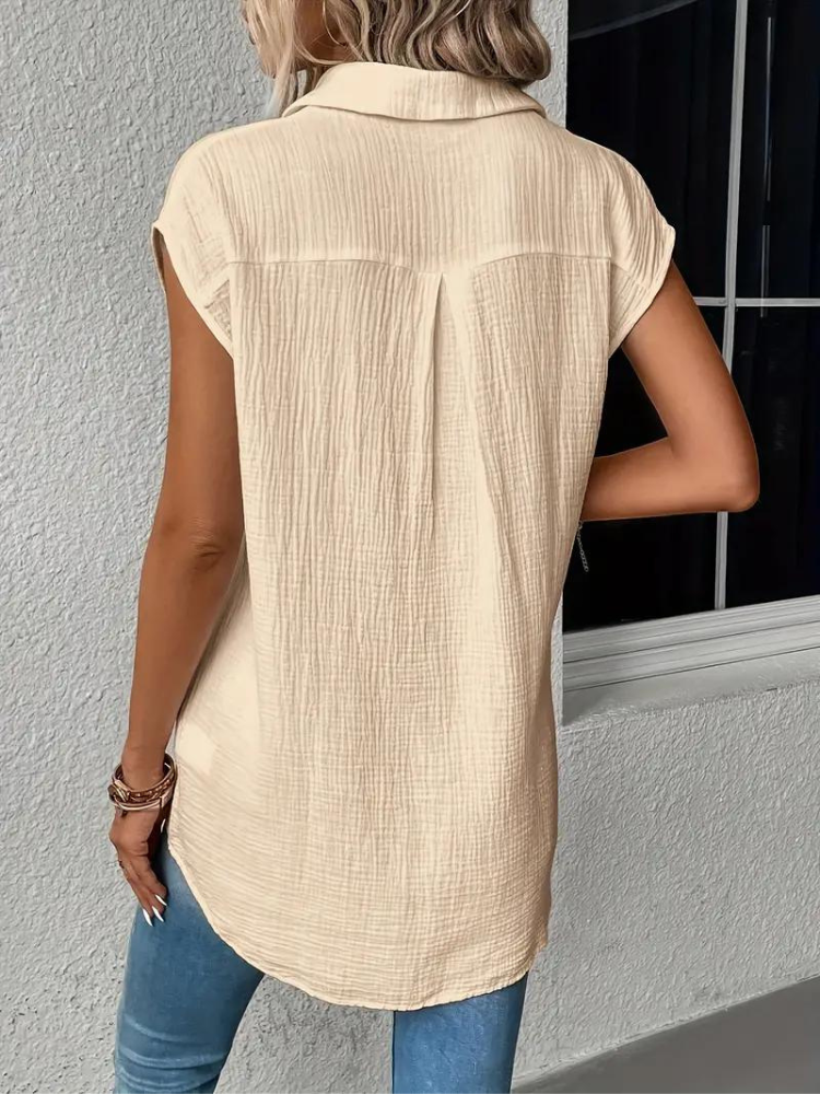 Femme portant une chemise beige à manches courtes, texture plissée, de dos, avec un jean bleu. Mode décontractée, style estival, tendance féminine.