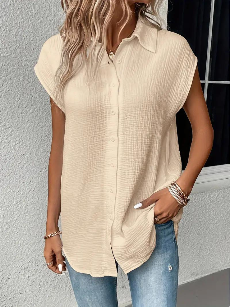 Femme portant une chemise beige texturée à manches courtes, col classique, associée à un jean bleu. Mode décontractée, tendance estivale.