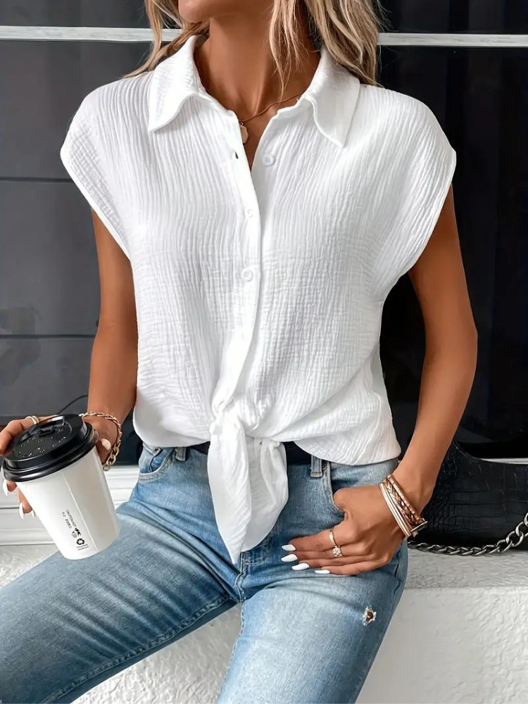 Femme portant une chemise blanche nouée, manches courtes, avec un jean bleu délavé, tenant un gobelet à café. Mode décontractée chic, style estival.