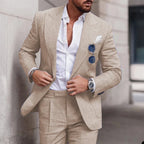 Homme en costume beige élégant, chemise blanche ouverte, lunettes de soleil accrochées, montre argentée, style mode masculine chic et moderne.