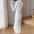 Robe longue blanche en tricot côtelé, manches longues, ajustée, élégante, portée par une femme dans un intérieur moderne avec parquet en bois.