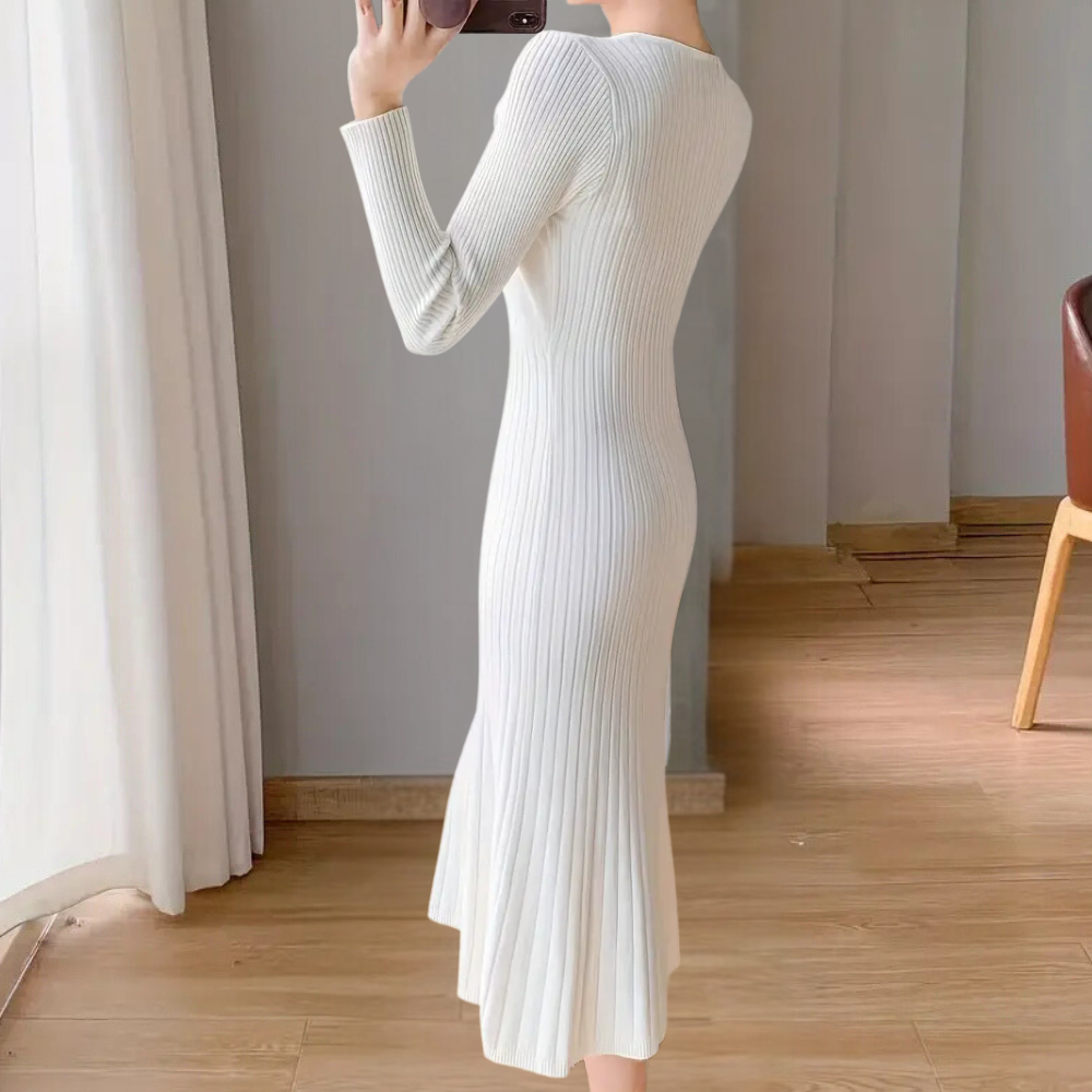 Robe longue blanche en tricot côtelé, manches longues, ajustée, élégante, portée par une femme dans un intérieur moderne avec parquet en bois.
