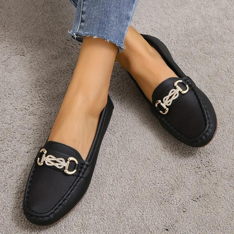 Chaussures mocassins noirs en cuir avec chaîne dorée, portés avec un jean bleu. Style élégant et moderne pour femmes.