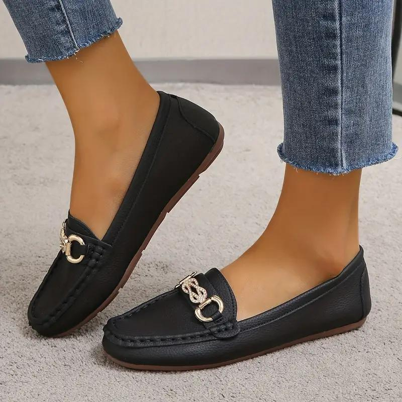 Mocassins noirs en cuir pour femme avec boucle dorée, portés avec un jean bleu. Chaussures élégantes et confortables pour un style décontracté.