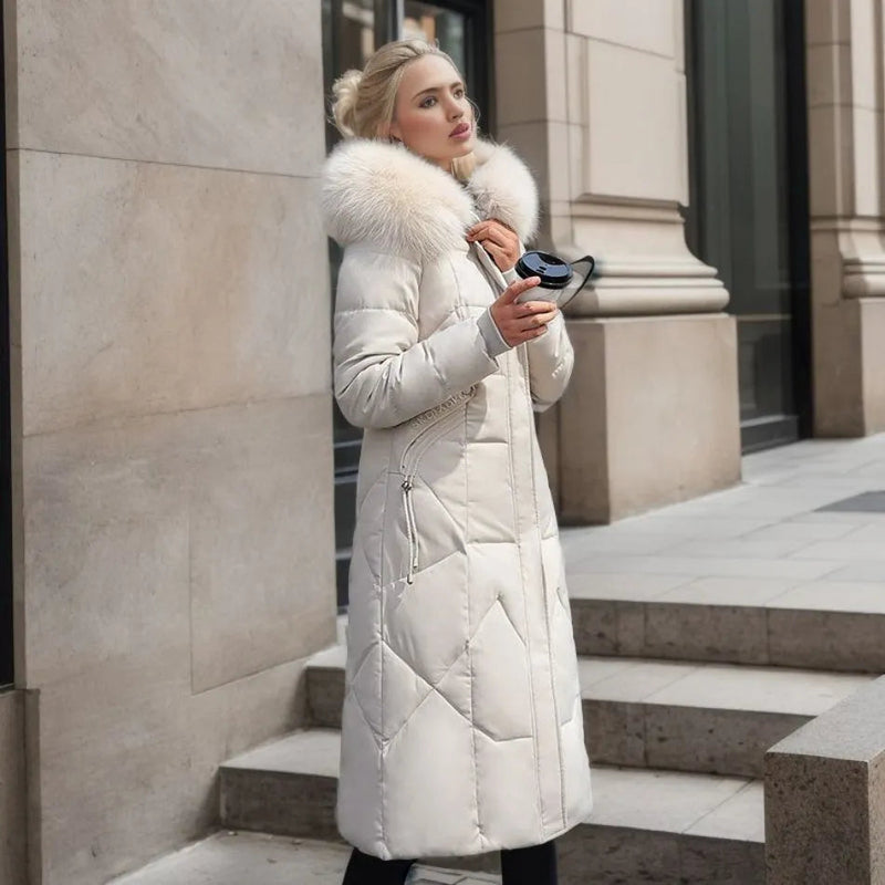 Femme portant un manteau d'hiver blanc avec col en fourrure, tenant un smartphone, debout devant un bâtiment urbain. Mode hiver élégante.
