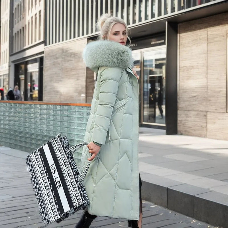 Femme en manteau d'hiver vert avec col en fourrure, tenant un sac à rayures noir et blanc, marchant en ville. Mode hiver, élégance urbaine.