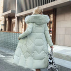 Femme en manteau long matelassé vert clair avec col en fourrure, marchant en ville. Mode hiver élégante, tendance manteaux femme, style urbain chic.
