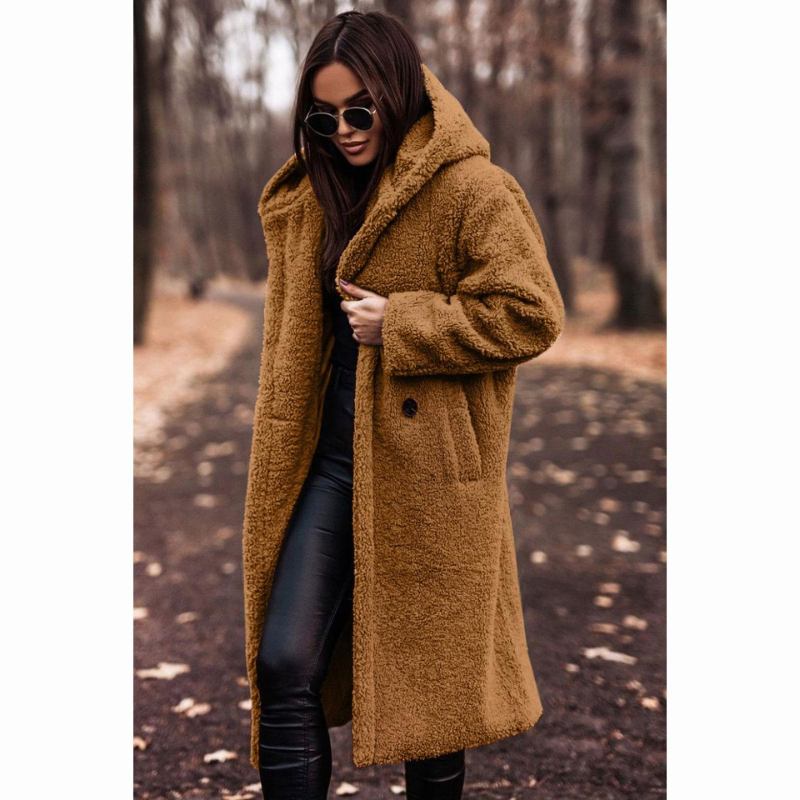 Femme portant un manteau en fausse fourrure marron, lunettes de soleil, sur un chemin forestier automnal. Mode hiver, style chic et tendance.