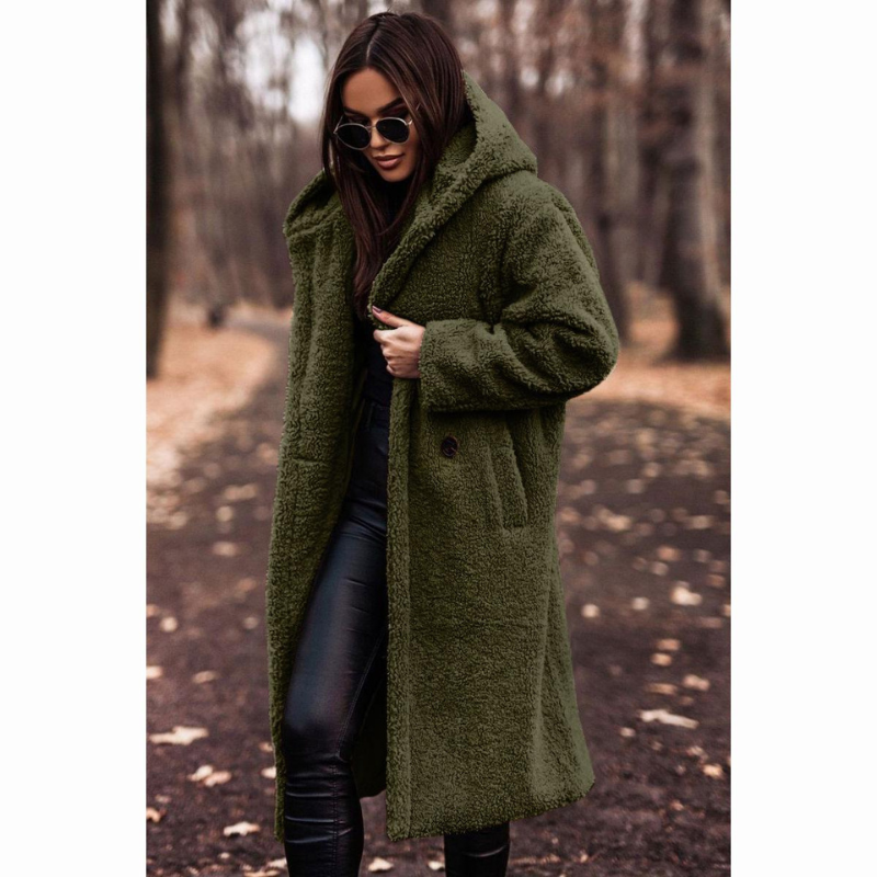 Femme portant un manteau en laine vert, lunettes de soleil, marchant dans une forêt automnale. Mode hiver, style chic, promenade nature.