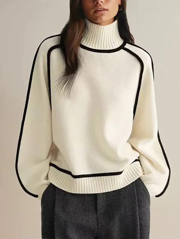 Femme portant un pull blanc à col roulé avec bordures noires, manches longues, associé à un pantalon gris. Mode automne-hiver élégante et moderne.