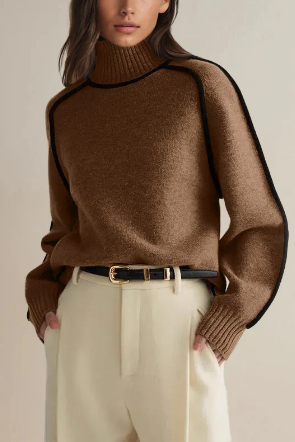 Femme portant un pull marron à col roulé avec bordures noires, associé à un pantalon beige taille haute. Mode automne-hiver élégante et chic.