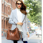 Femme élégante en manteau gris, portant un sac à main en cuir marron, lunettes de soleil, marchant en ville. Mode automne, style urbain chic.