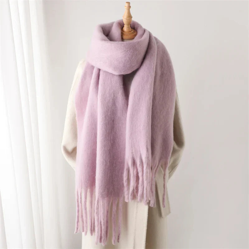 Écharpe en laine rose pâle avec franges, posée sur un mannequin beige. Accessoire mode hiver, doux et élégant, idéal pour temps froid.