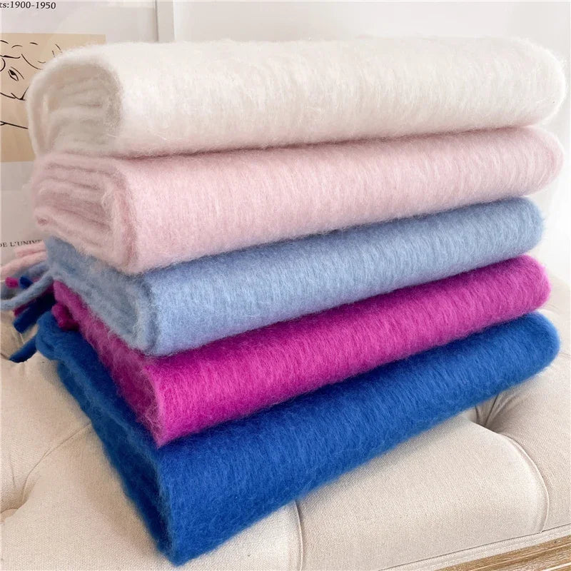 Cinq écharpes en mohair empilées, couleurs blanc, rose, bleu clair, fuchsia et bleu, sur un canapé beige. Accessoires mode hiver doux et chauds.