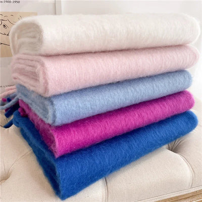 Cinq écharpes en mohair empilées, couleurs blanc, rose, bleu clair, fuchsia et bleu, sur un canapé beige. Accessoires mode hiver doux et chauds.