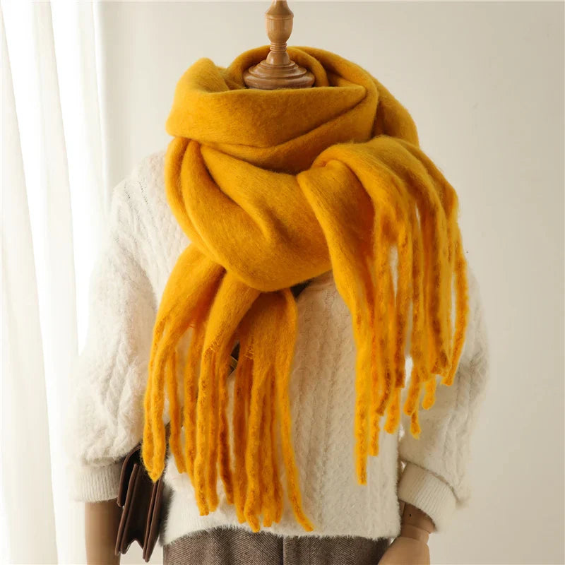 Écharpe jaune en laine épaisse avec franges, posée sur un mannequin habillé d'un pull blanc texturé. Accessoire mode hiver chaud et tendance.