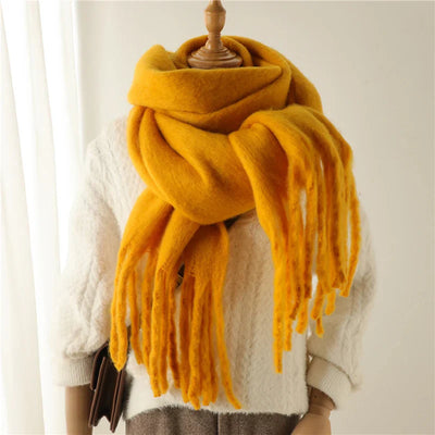 Écharpe jaune en laine épaisse avec franges, posée sur un mannequin habillé d'un pull blanc texturé. Accessoire mode hiver chaud et tendance.
