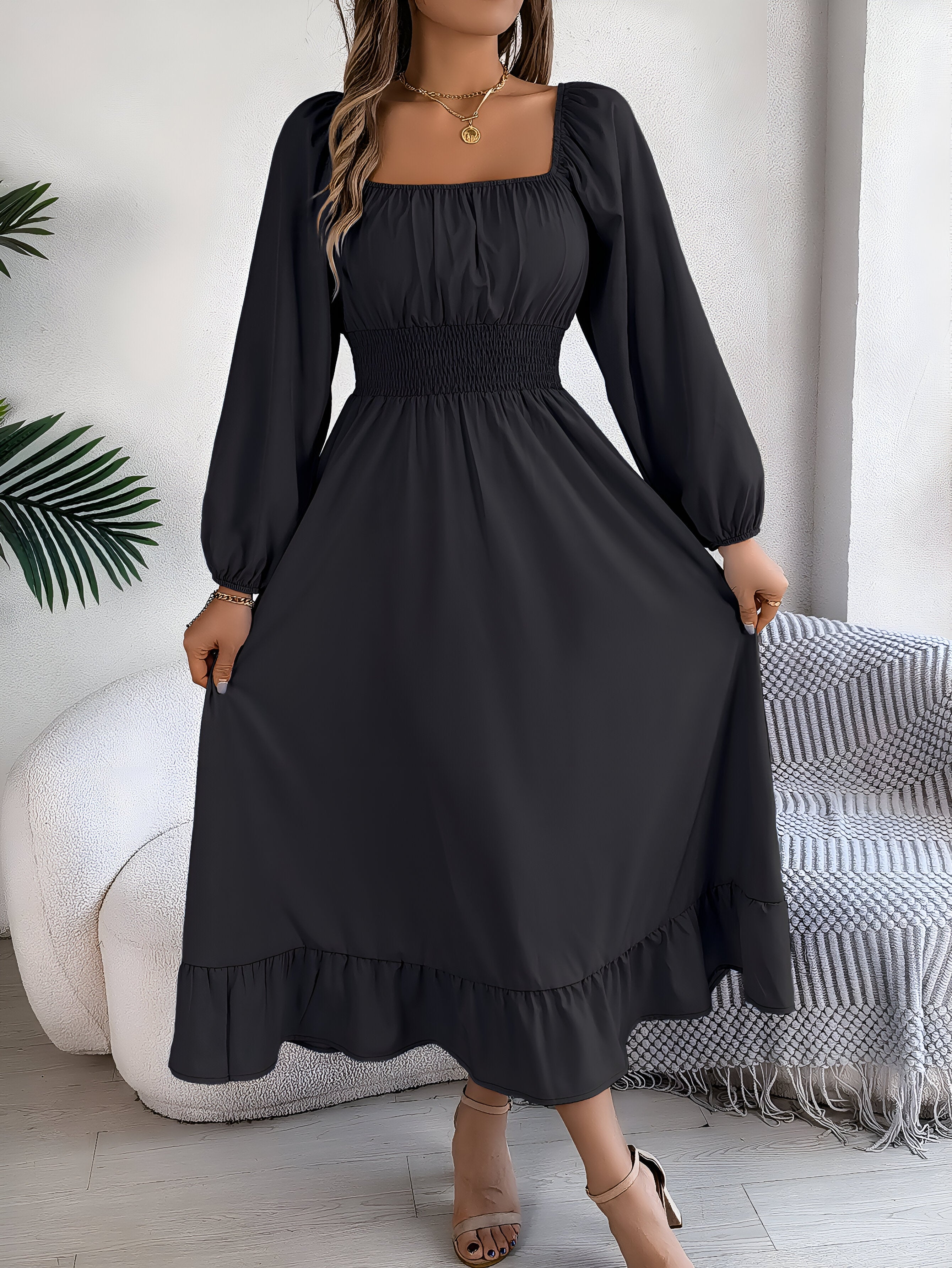 Robe longue noire à manches longues, col carré, taille froncée, portée par une femme. Style élégant et moderne, idéal pour soirées ou occasions spéciales.
