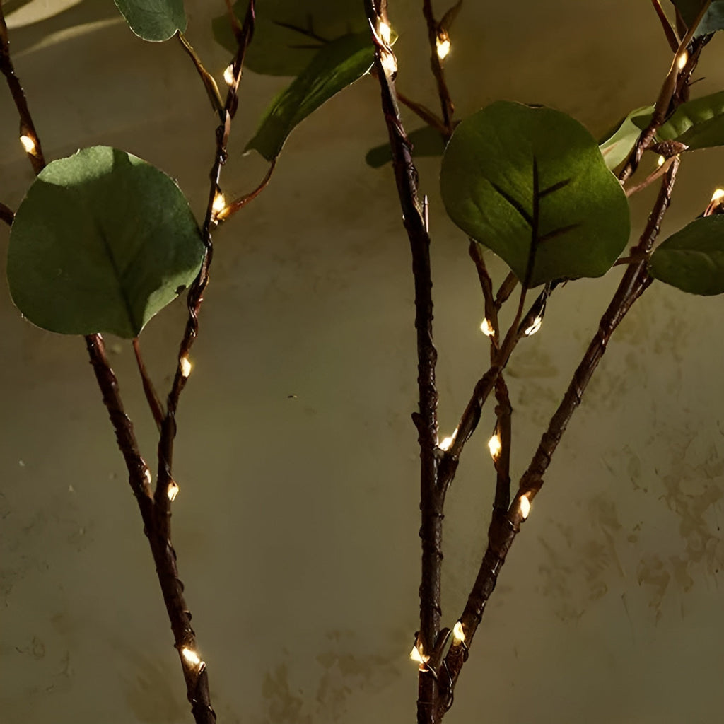 Branche décorative avec feuilles vertes et guirlande lumineuse LED, éclairage d'ambiance intérieur, décoration naturelle et moderne.