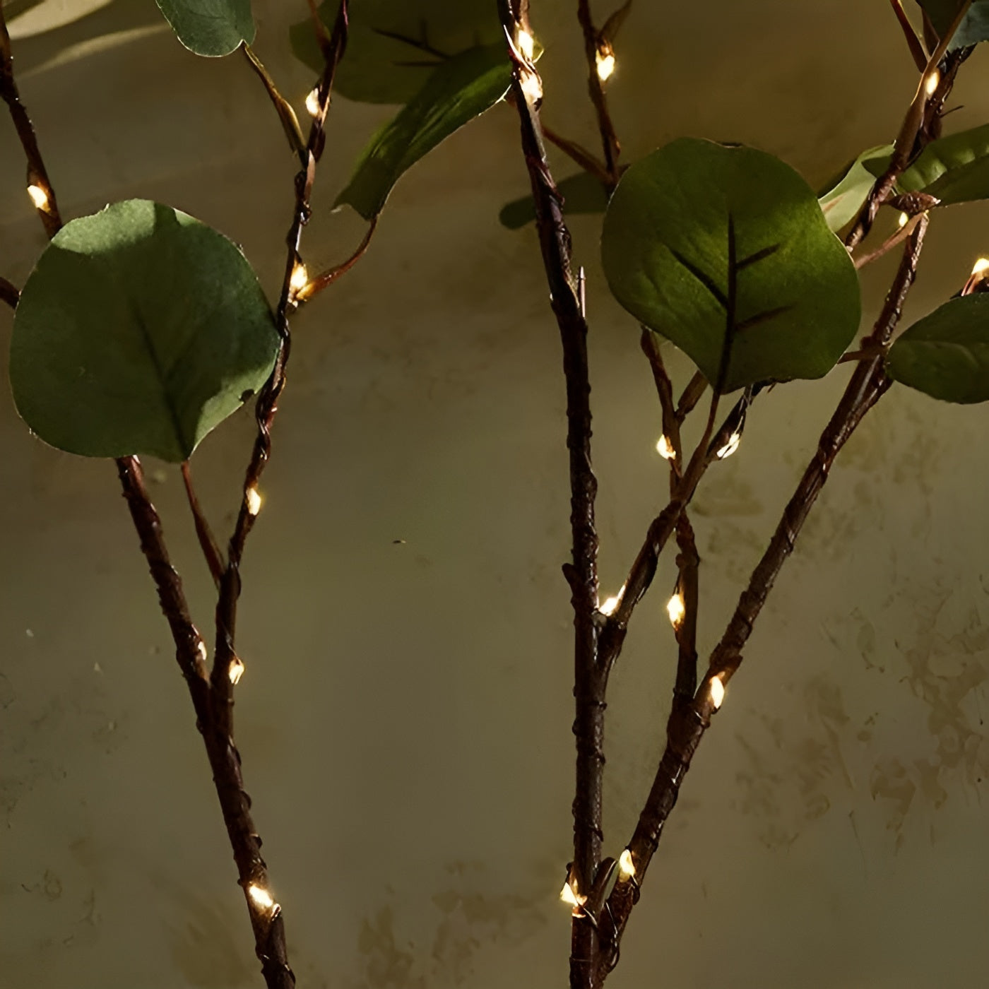 Branche décorative avec feuilles vertes et guirlande lumineuse LED, éclairage d'ambiance intérieur, décoration naturelle et moderne.