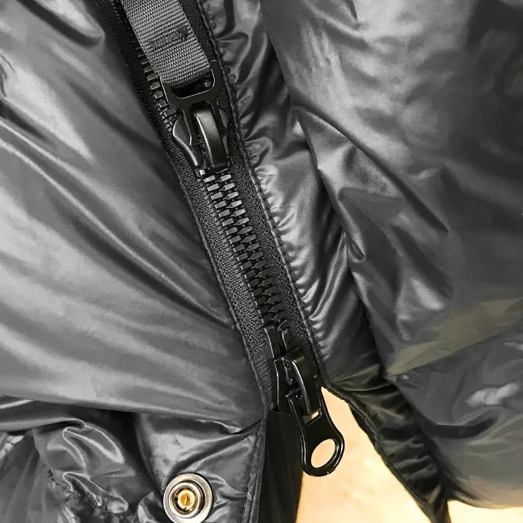 Gros plan d'une fermeture éclair noire sur une veste en nylon imperméable, texture brillante. Mode hiver, vêtement chaud, détail pratique.