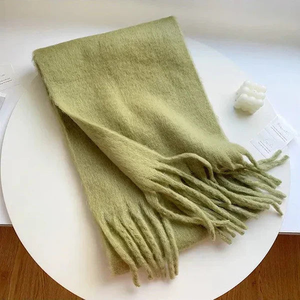 Écharpe en laine verte posée sur une table blanche, avec franges élégantes. Accessoire mode hiver, doux et chaud, idéal pour un look tendance.