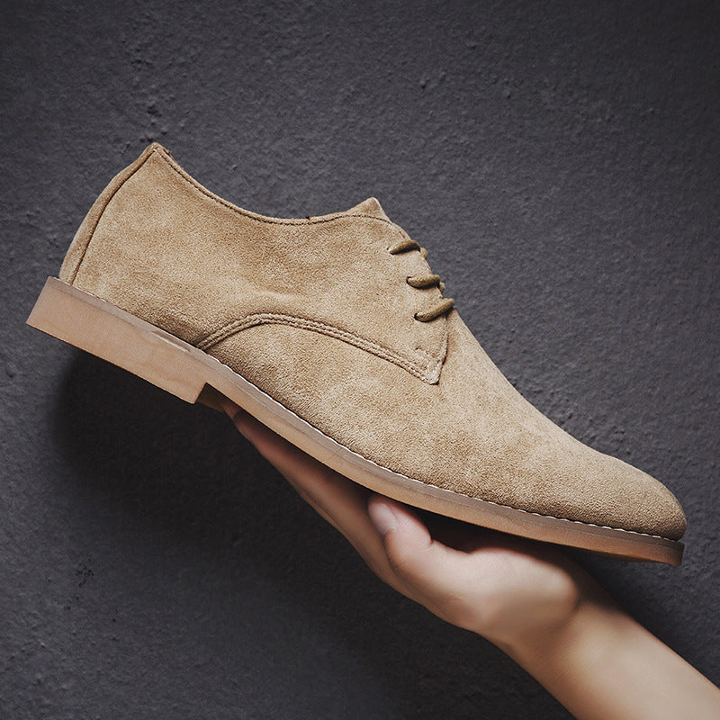 Chaussure derby en daim beige tenue en main, semelle marron clair, style élégant et moderne, idéale pour mode masculine et occasions formelles.