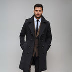 Homme élégant en manteau noir, costume marron et cravate, posant sur fond gris. Mode masculine, style formel, tendance automne-hiver.