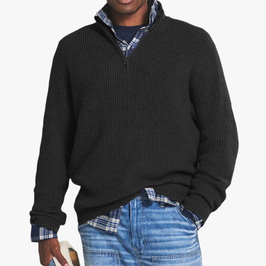 Homme portant un pull noir à col zippé sur une chemise à carreaux bleue, avec un jean décontracté. Mode masculine automne-hiver, style décontracté.