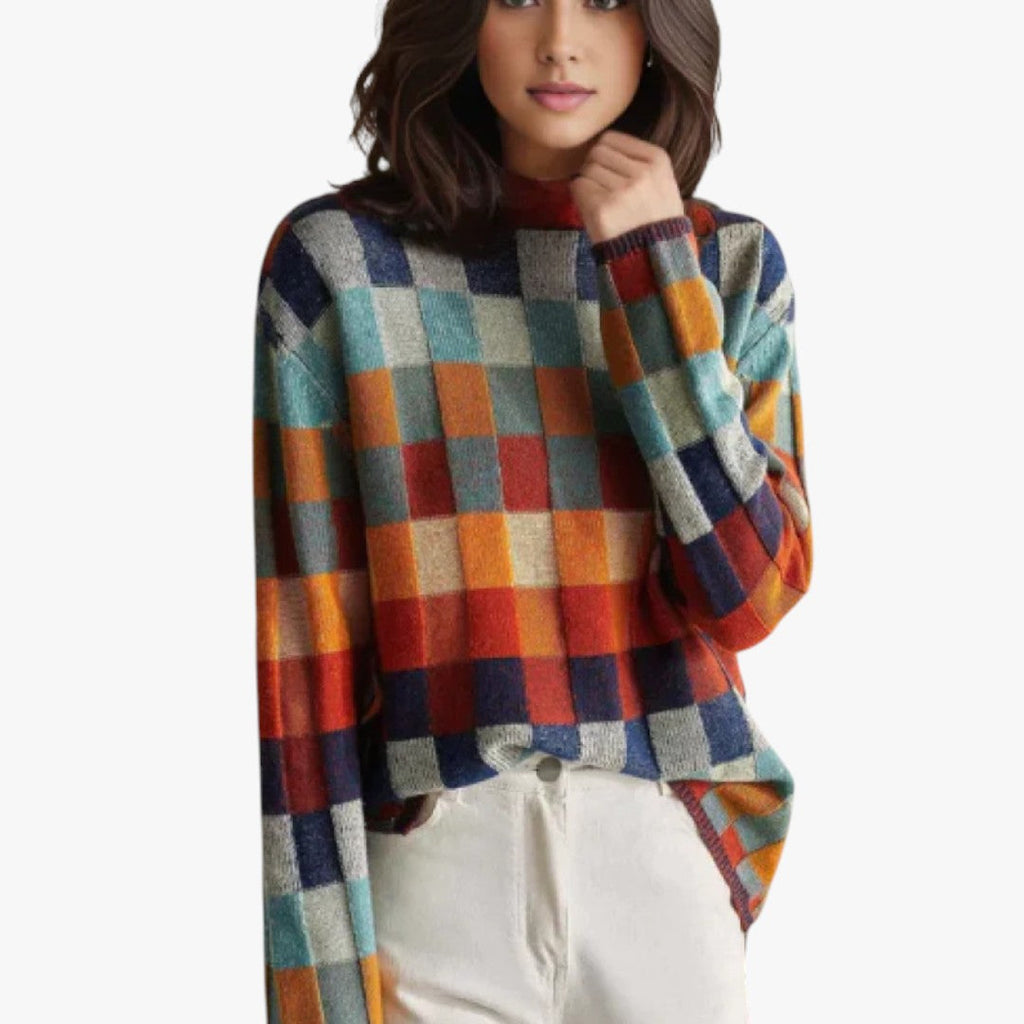 Femme portant un pull à carreaux multicolores, manches longues, col rond, avec un pantalon blanc. Mode automne-hiver, style décontracté et tendance.