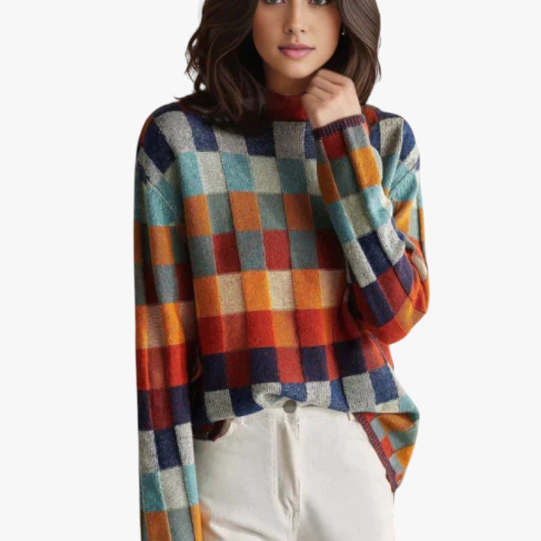 Femme portant un pull à carreaux multicolores, manches longues, col rond, avec un pantalon blanc. Mode automne-hiver, style décontracté et tendance.