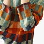 Pull à carreaux multicolores en laine, manches longues, motifs géométriques, tons orange, bleu et vert, mode automne-hiver, style décontracté.