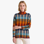 Femme portant un pull à col roulé à carreaux multicolores, fond blanc. Mode automne-hiver, style décontracté, tendance vêtements chauds.
