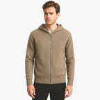 Homme portant un cardigan à capuche beige, fermeture éclair, sur fond blanc. Mode masculine, vêtement décontracté, style automne-hiver.