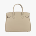 Sac à main beige en cuir texturé, style Birkin, avec poignées doubles et pieds métalliques dorés. Accessoire de mode élégant et luxueux.