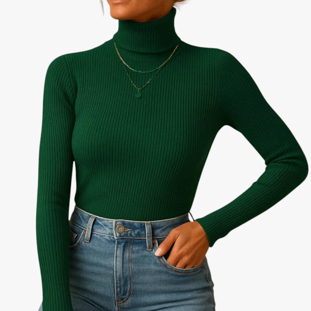 Femme portant un pull col roulé vert foncé côtelé, manches longues, avec un jean taille haute bleu et un collier délicat. Mode automne-hiver tendance.