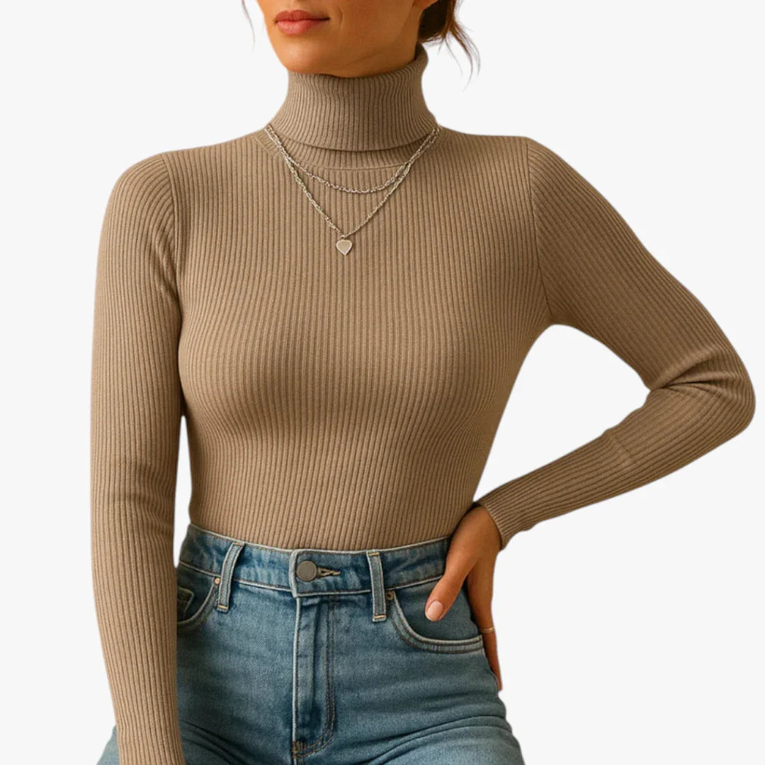 Femme portant un pull col roulé beige côtelé, manches longues, avec colliers superposés, associée à un jean taille haute bleu. Mode automne chic.